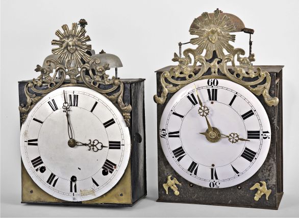 (1) France, Comtoise clock, 8 day, time and quarter strike, weight driven movement with verge escapement, thread suspension with rear-hanging pendulum in an iron post and plate frame, convex white enamel dial with Roman numerals for the hours, two pierced brass hands, cast bronze fronton featuring the sun and/or Apollo, flowers, and a sheaf of wheat, c1800; (2) France, month-running Comtoise clock, 30 day, time and strike with alarm, weight driven movement with verge escapement, thread suspension with front-hanging pendulum in a posted iron case, convex faïence dial with Roman numerals for the hours, and Arabic numerals at the quarters, brass alarm ring with Arabic numerals, two brass hands, cast eagle spandrels, and cast fronton with central sun and eagle images, c1810.