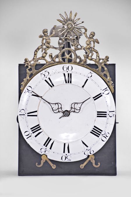 France, month-running Comtoise clock, 30 day, time and strike, weight driven movement, verge escapement with thread suspension and rear-hanging pendulum in an iron post and plate frame, white enamel dial with concave center and convex chapter, Roman numerals for the hours and Arabic numerals every five minutes, two pierced iron hands, pivoted brass winding arbor shutters below the dial, all topped by a cast fronton featuring the sun flanked by putti and displaying the star symbol used during the French Restoration Period.