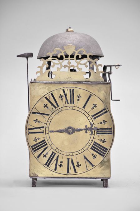 France, lantern clock, 30 hour, time and strike, weight driven movement, verge escapement with upward facing crown wheel, thread suspension with side-mounted pendulum, posted iron frame resting on short iron feet, brass front with integrated dial showing Roman numerals, single iron hand, topped by bell and pierced brass fronton.