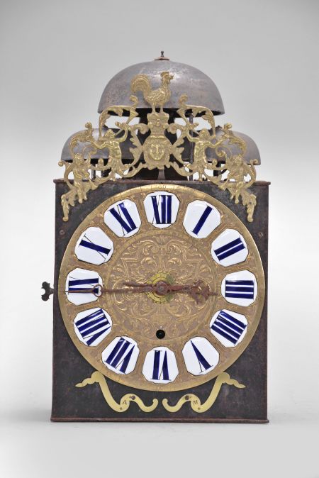 France, bronze-front Comtoise clock, 8 day, time and quarter strike with alarm, three bells, weight driven movement with verge escapement, thread suspension with rear-hanging pendulum in an iron post and plate frame, cast brass dial inset with 12 white enamel cartouches showing Roman numerals, Arabic numerals at 5 minute intervals on the outer rim, brass alarm ring with Arabic numerals, two iron hands, pivoted brass winding arbor shutters engraved with "A" and "M", all topped by cast fronton depicting trumpeters flanking a small forward facing Gallic rooster.