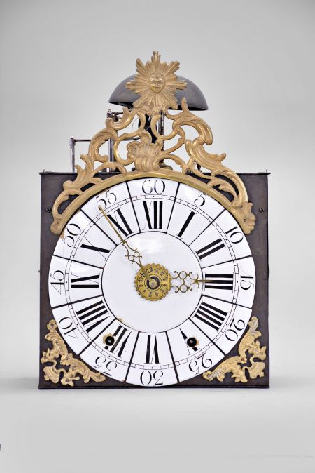 France, Louis XV Comtoise clock, 8 day, time and strike with alarm, weight driven movement with verge escapement, thread suspension with rear-hanging pendulum, iron post and plate frame, dial composed of 13 enamel panels with Roman and Arabic numerals, brass alarm ring with Arabic numerals, two pierced brass hands, cast brass spandrels below the dial with putti supporting crowns, all topped by a cast brass fronton with sun emblem within a rococo design.