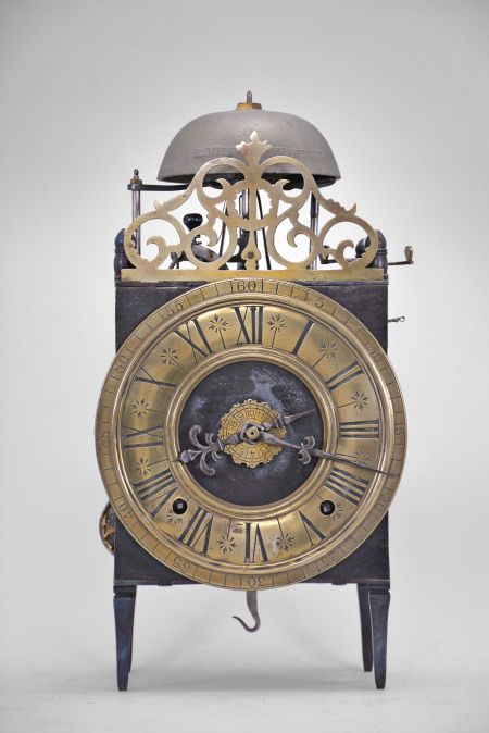 France, Comtoise lantern clock, 8 day, time and strike with alarm, weight driven movement with Chevalier de Béthune escapement, thread suspension with rear-hanging pendulum in a iron posted iron frame, brass chapter ring with engraved Roman numerals, brass alarm ring with engraved Arabic numerals, two iron hands, all surmounted by a cast brass fronton and four turned iron finials.