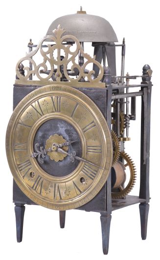 France, Comtoise lantern clock, 8 day, time and strike with alarm, weight driven movement with Chevalier de Béthune escapement, thread suspension with rear-hanging pendulum in a iron posted iron frame, brass chapter ring with engraved Roman numerals, brass alarm ring with engraved Arabic numerals, two iron hands, all surmounted by a cast brass fronton and four turned iron finials.