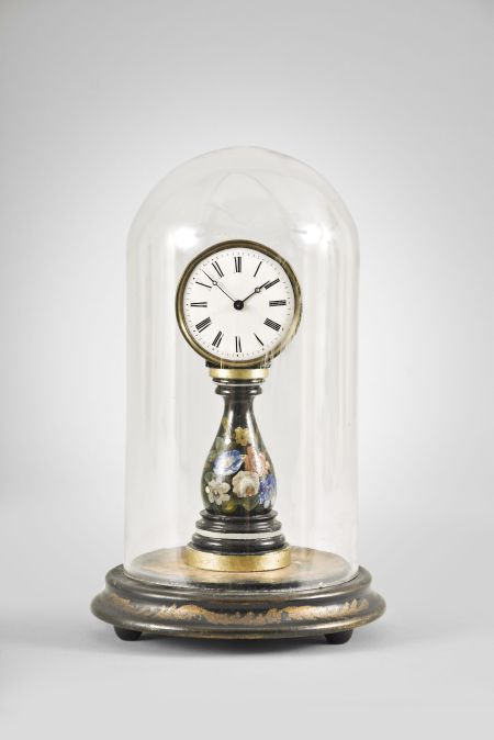 A small, European candlestand clock, ebonized baluster form base with floral decoration supporting a roman numeral white enamel dial with blued steel Breguet style hands, 30 hour timepiece movement with tic tac escapement, all mounted to a decorated turned wooden base with glass dome