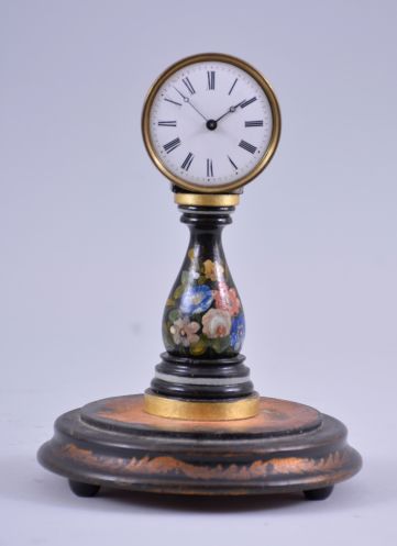 A small, European candlestand clock, ebonized baluster form base with floral decoration supporting a roman numeral white enamel dial with blued steel Breguet style hands, 30 hour timepiece movement with tic tac escapement, all mounted to a decorated turned wooden base with glass dome