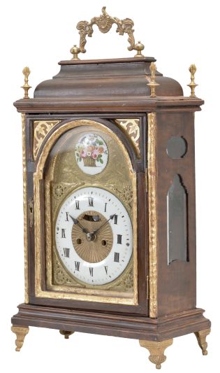 Austria, a late 18th century bracket clock, the molded base with cast, gilt feet, faux arch door with fabric backed frets at the upper corners, and caddy top, surrounded by four finials and with carrying handle, engraved brass dial with roman numeral, white enamel chapter ring, surrounded by cast spandrels, blued steel hands, patterned center with aperture for observation of mock pendulum, and boss in the arch with polychrome enamel scene with bird and basket of flowers, two train, two day movement with crown wheel escapement and rack striking, sounding the hours on a bell