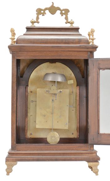 Austria, a late 18th century bracket clock, the molded base with cast, gilt feet, faux arch door with fabric backed frets at the upper corners, and caddy top, surrounded by four finials and with carrying handle, engraved brass dial with roman numeral, white enamel chapter ring, surrounded by cast spandrels, blued steel hands, patterned center with aperture for observation of mock pendulum, and boss in the arch with polychrome enamel scene with bird and basket of flowers, two train, two day movement with crown wheel escapement and rack striking, sounding the hours on a bell