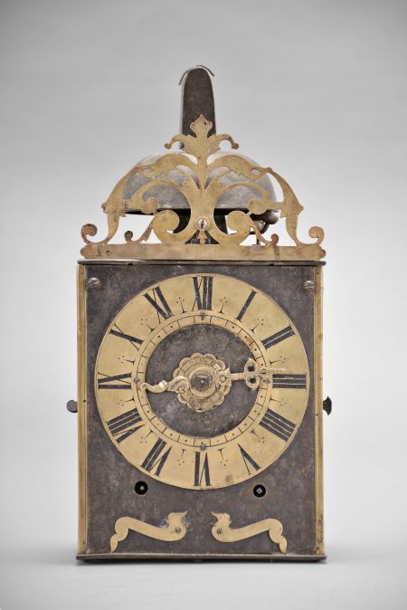 France, Comtoise clock, 8 day, time and strike with alarm, weight driven movement with verge escapement, thread suspension with rear-hanging pendulum in a iron post and plate frame, brass chapter ring with engraved Roman numerals, brass alarm ring with engraved Arabic numerals, pivoted winding arbor shutters, single pierced brass hand, the top with pierced brass fronton.